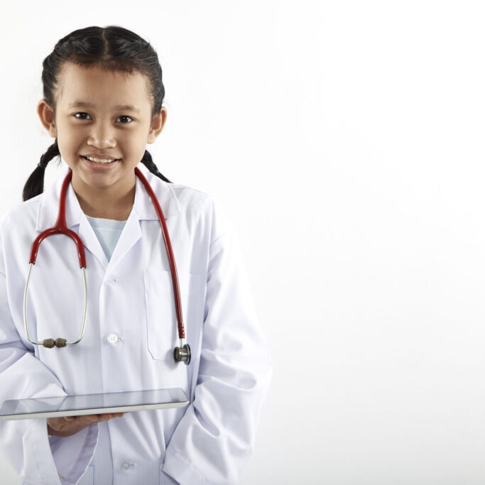 Cute Asian little girl in doctor costume with stethoscope and tablet smiling and looking away on white background, Health care concept